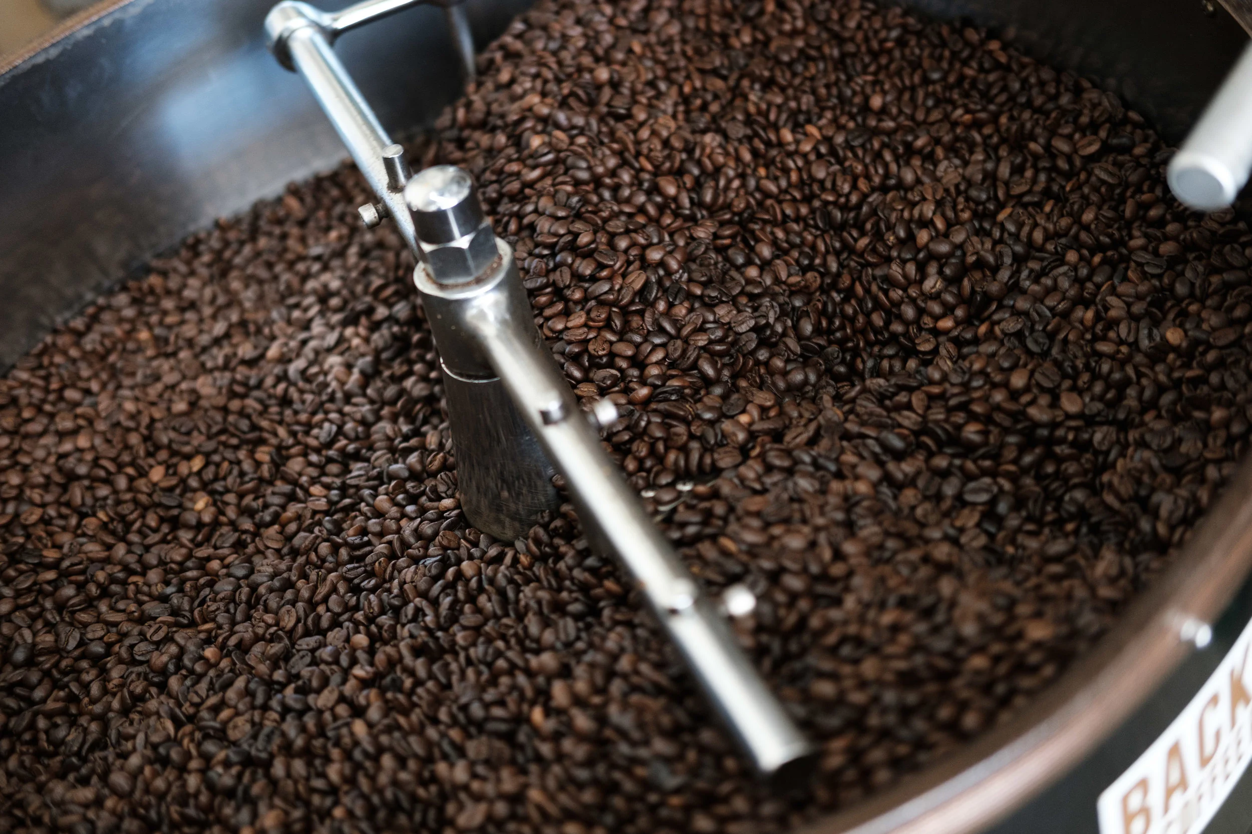Dark roasted coffee beans in a metal roaster machine.