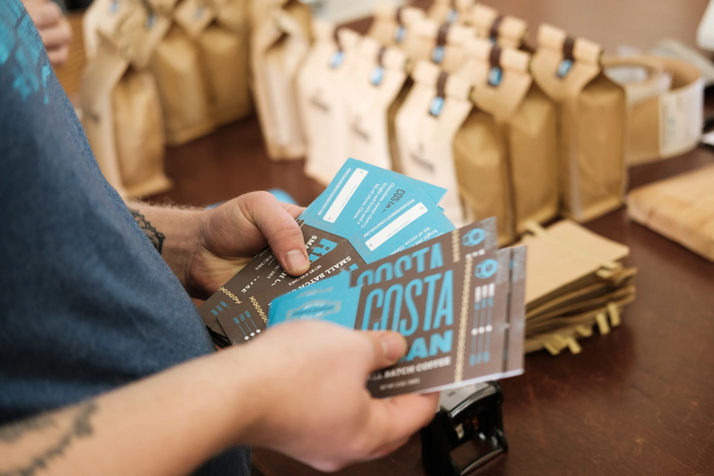 Person holding two blue and black event tickets for Costa Vegan, with brown paper packets in the background.