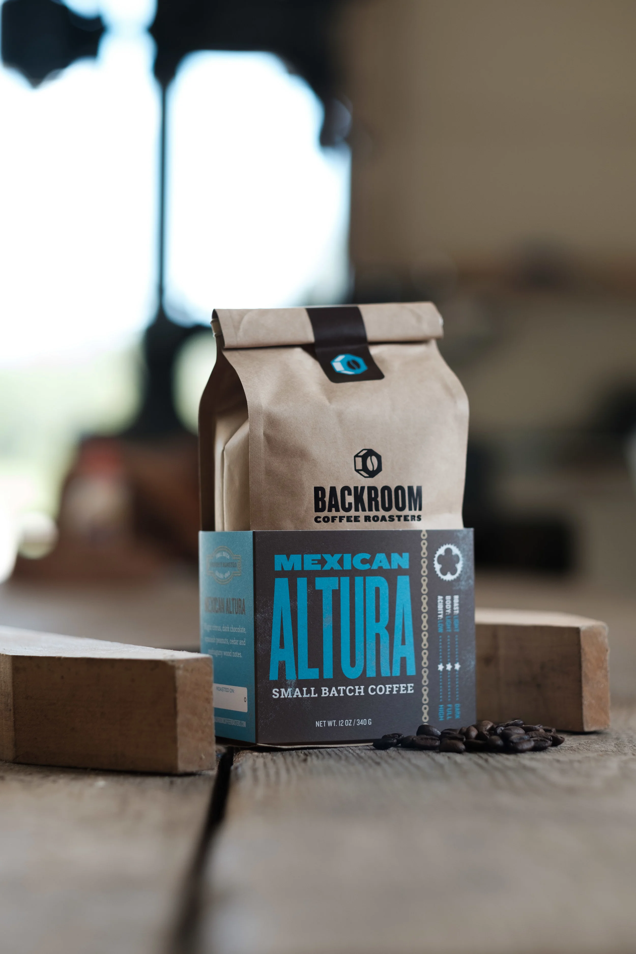 A bag of Mexican Altura small batch coffee from Backroom Coffee Roasters, placed on a wooden surface with coffee beans in front of it.