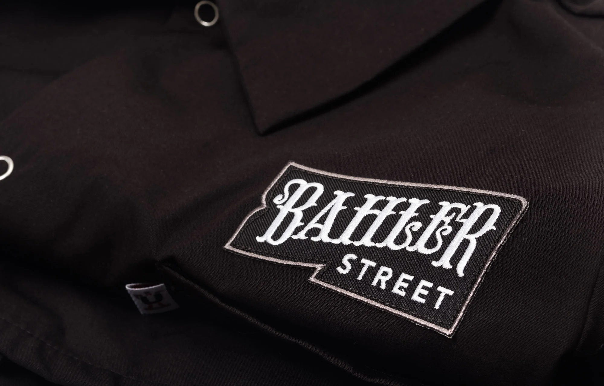 Close-up of a black backpack with a patch that reads 'BASICS STREET' in white and black embroidery.