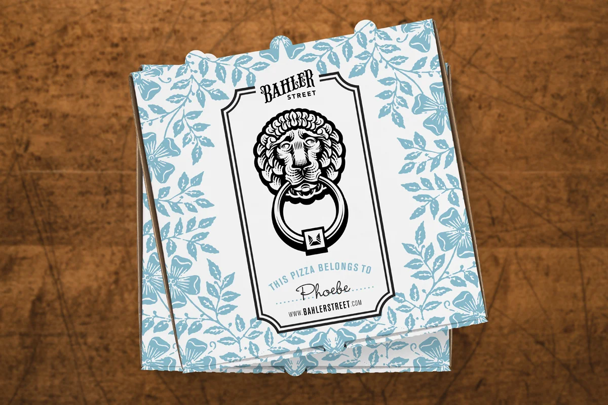 A pizza box from Bahler Street featuring a tiger head door knocker graphic, blue floral and butterfly pattern, and a personalized message with the name Phoebe.