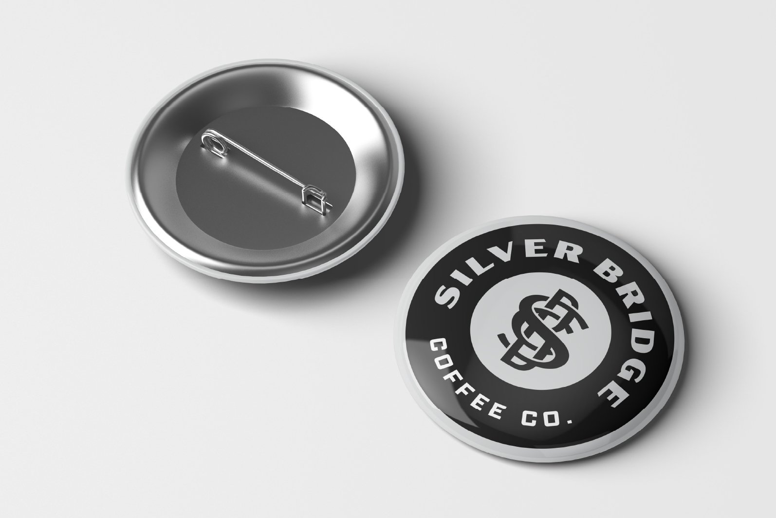 Silver button badge with 'Silver Bridge Coffee Co.' logo, and a safety pin on the back for attachment.