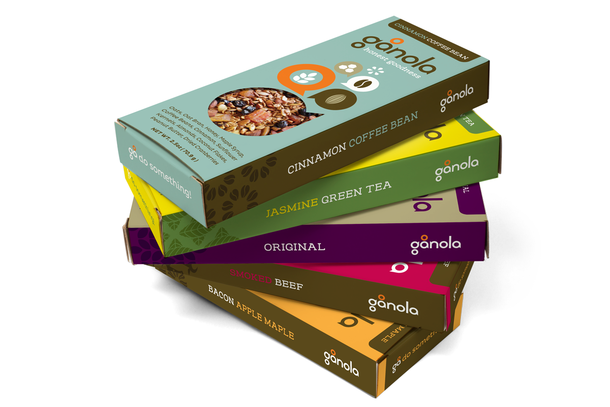 Stacked boxes of Ganola snack bars with flavors including cinnamon coffee bean, jasmine green tea, original, smoked beef, and bacon apple maple.