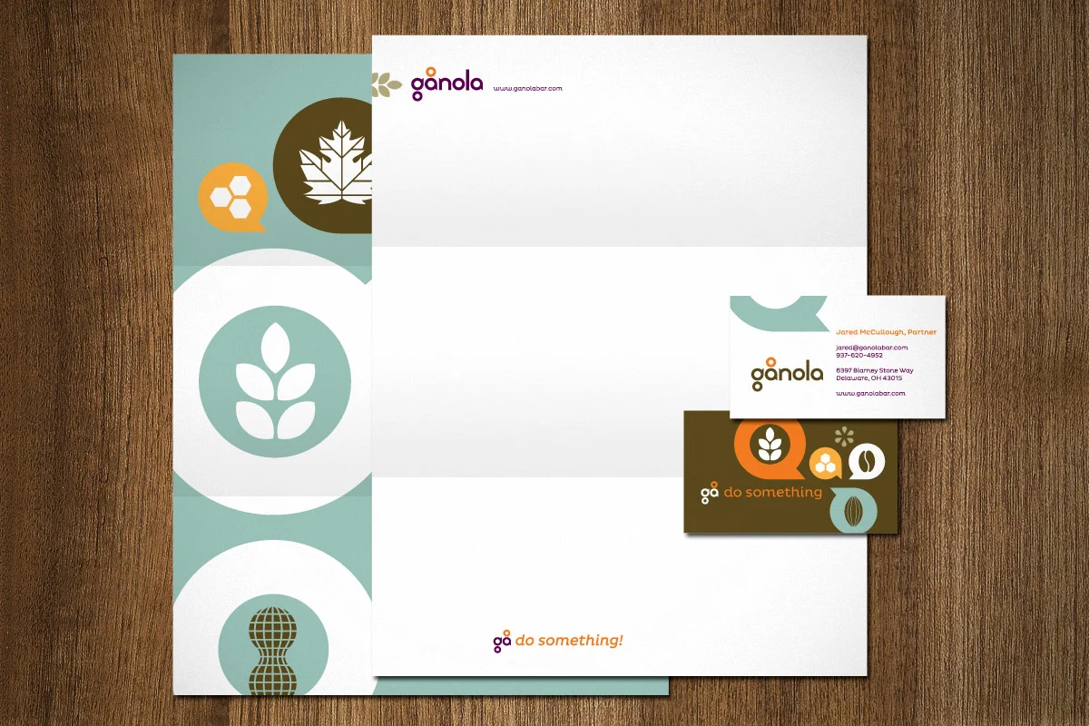 Set of branding materials for Ganola, including a letterhead, business card, and a brochure or flyer, with icons and logos featuring a leaf and Earth motifs in green, orange, and white colors, placed on a wooden surface.