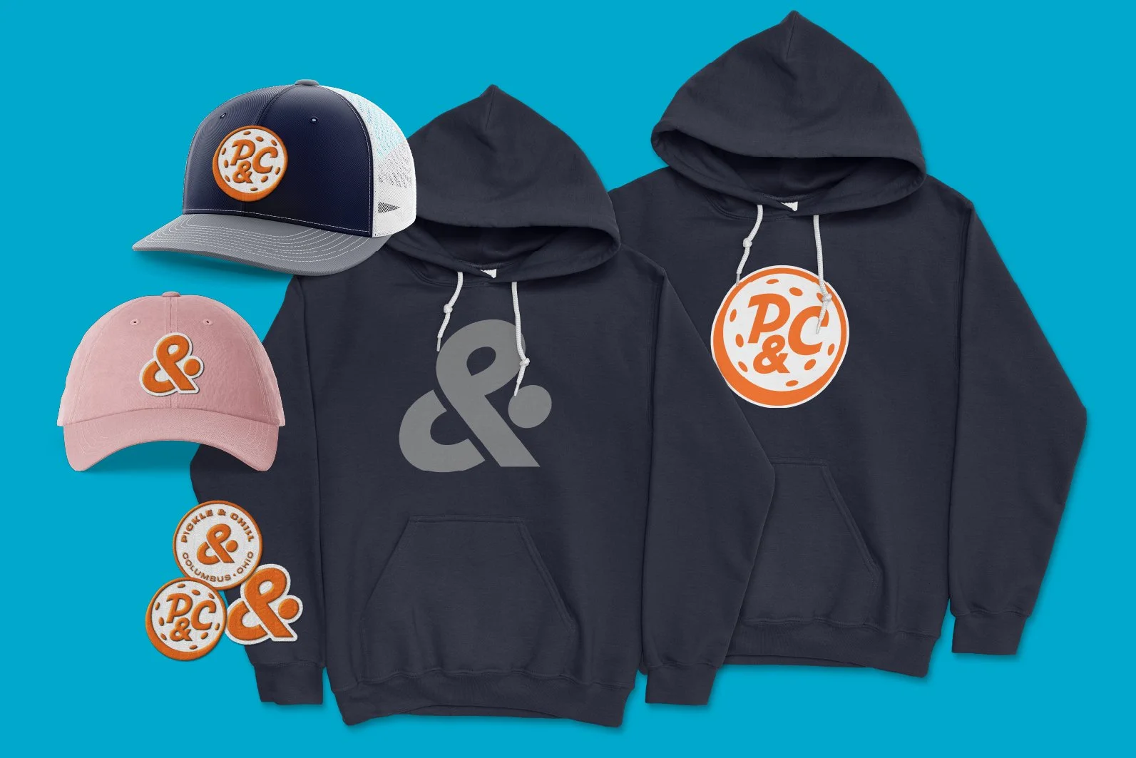 Collection of branded clothing and accessories on a blue background, including two black hoodies with large logo prints, two caps with logo patches, and several patches and buttons with logo designs.