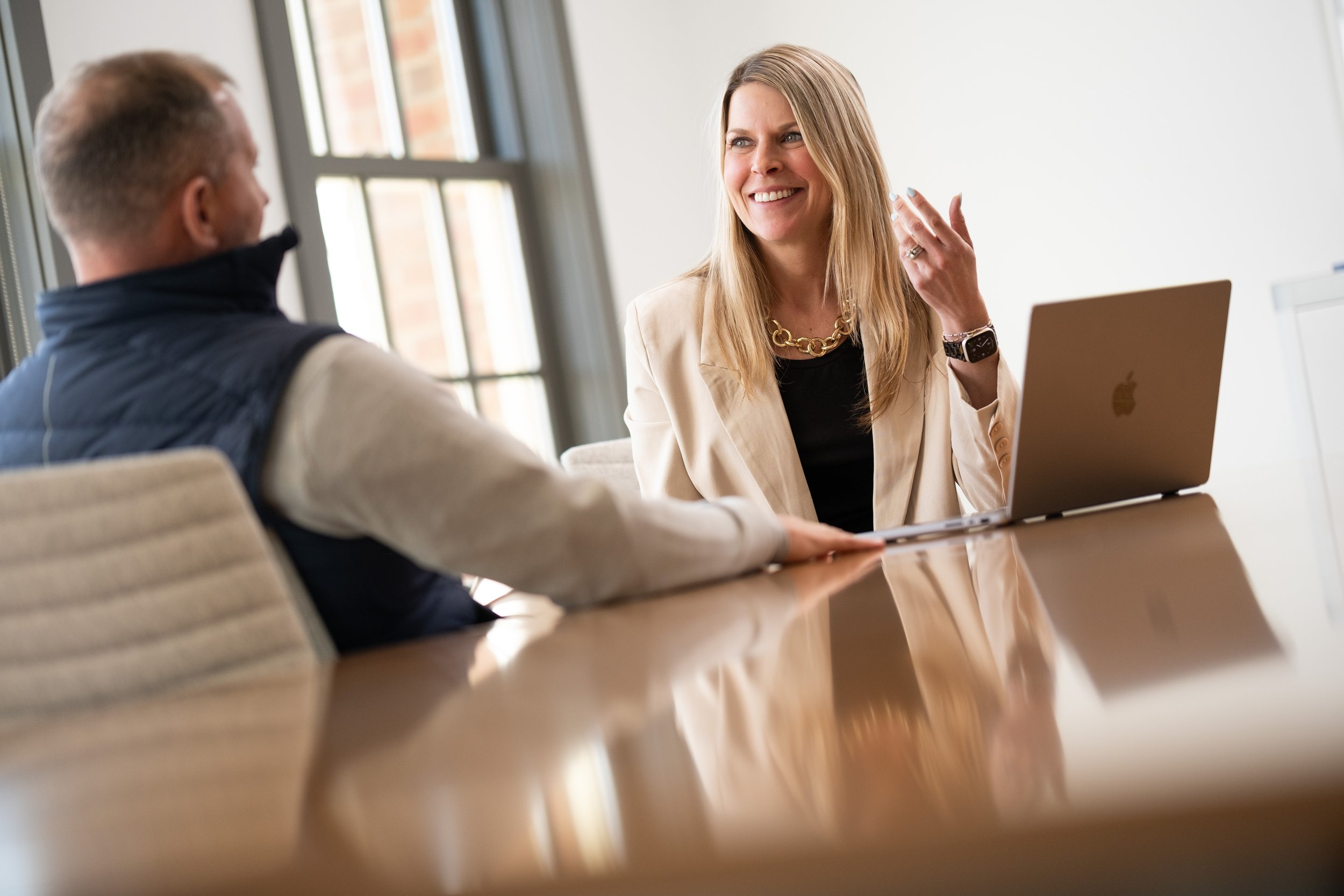 A woman and a man having a conversation in an office, with a laptop on the table.