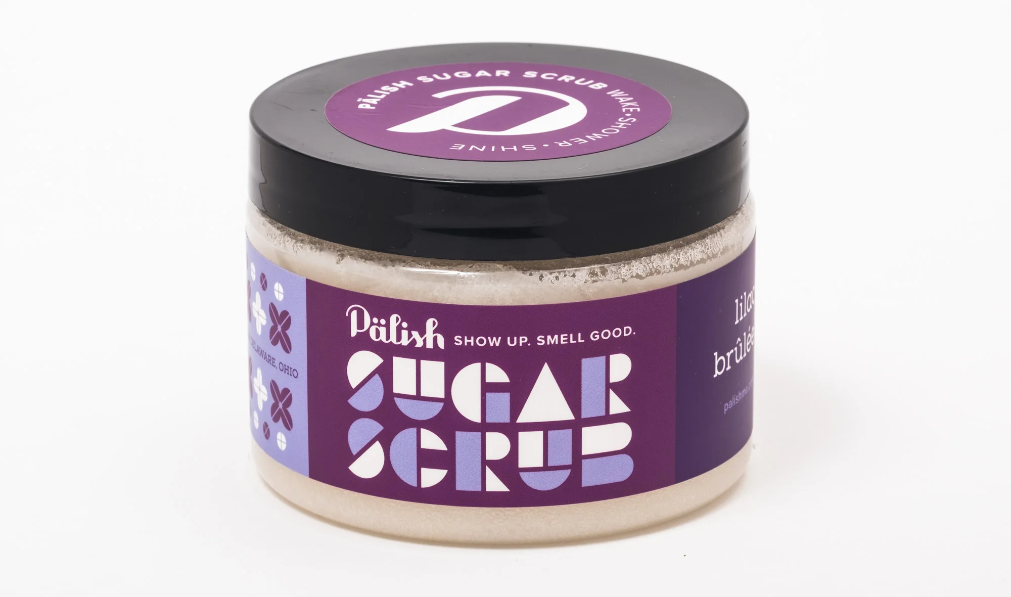 A jar of Pâlish sugar scrub with a purple label and black lid, featuring white and purple text and floral patterns.
