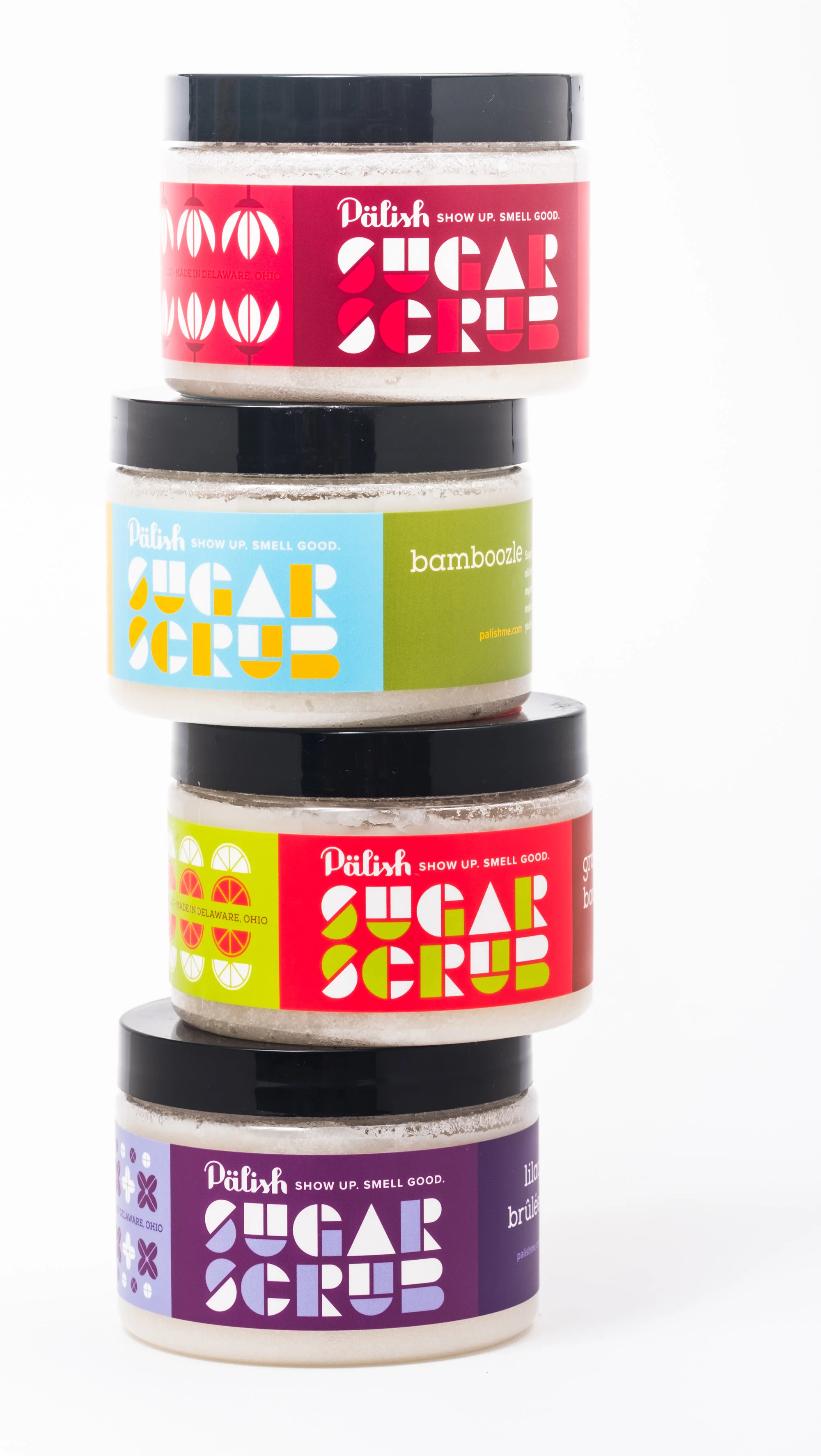 Stacked jars of sugar scrubs with colorful labels and black lids.