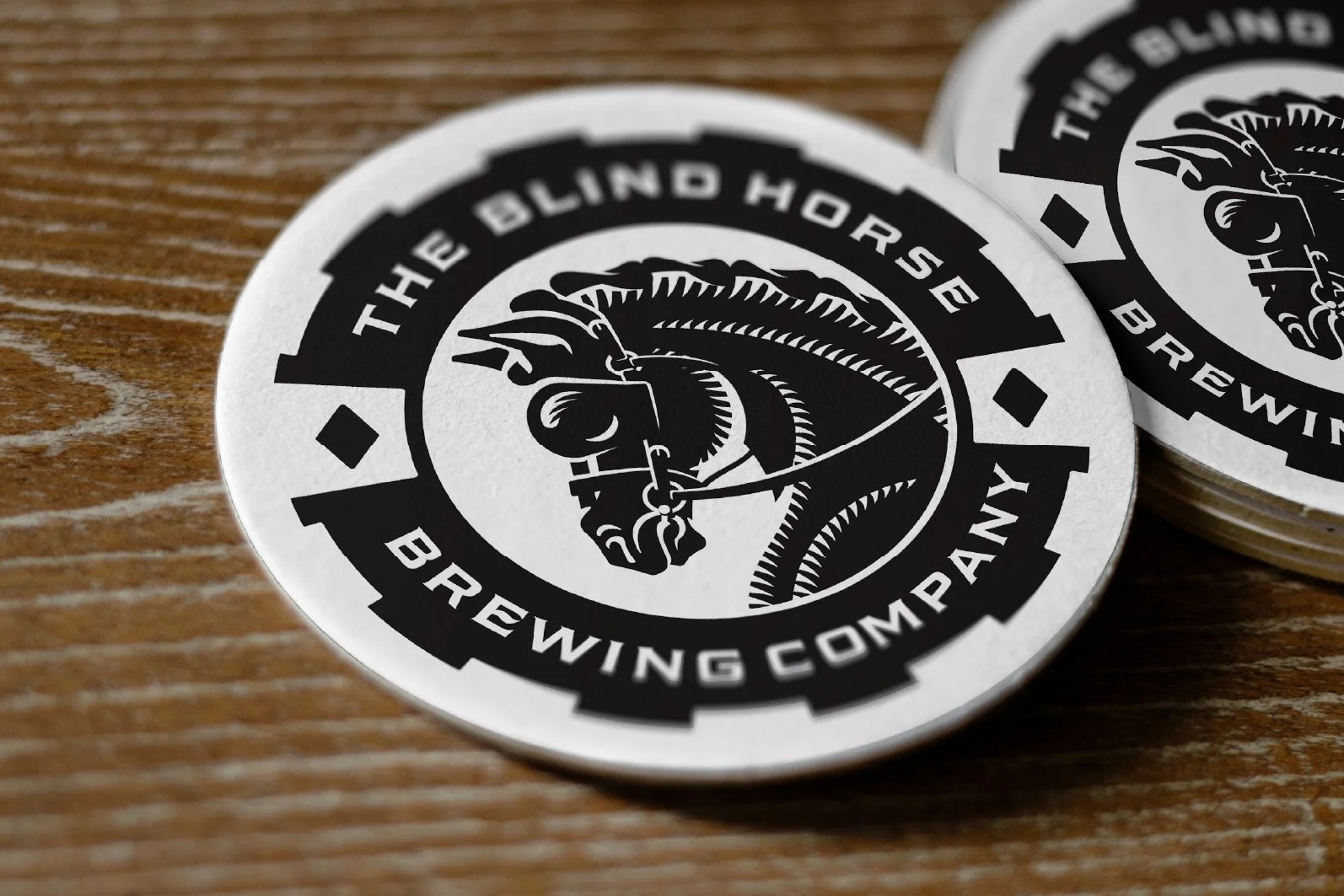 Close-up of a round sticker with a black and white design featuring a knight's helmet and the text 'The Blind Horse Brewing Company' on a wooden surface.
