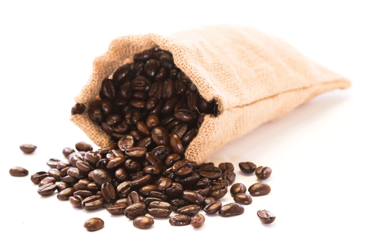 A burlap sack filled with roasted coffee beans spilling onto a white surface.