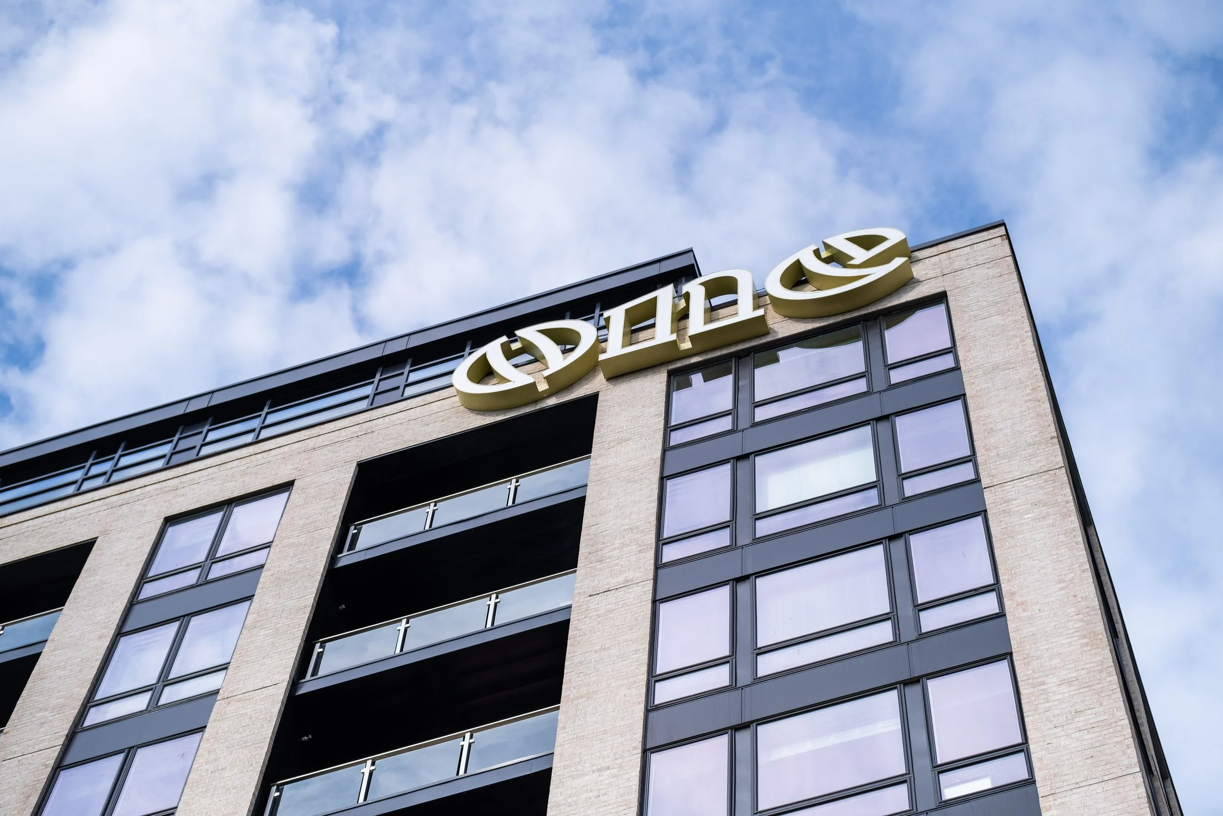 A modern multi-story building with a sign at the top displaying the word 'Silex' in large gold letters. The building has large glass windows and a brick facade, with a partly cloudy sky in the background.