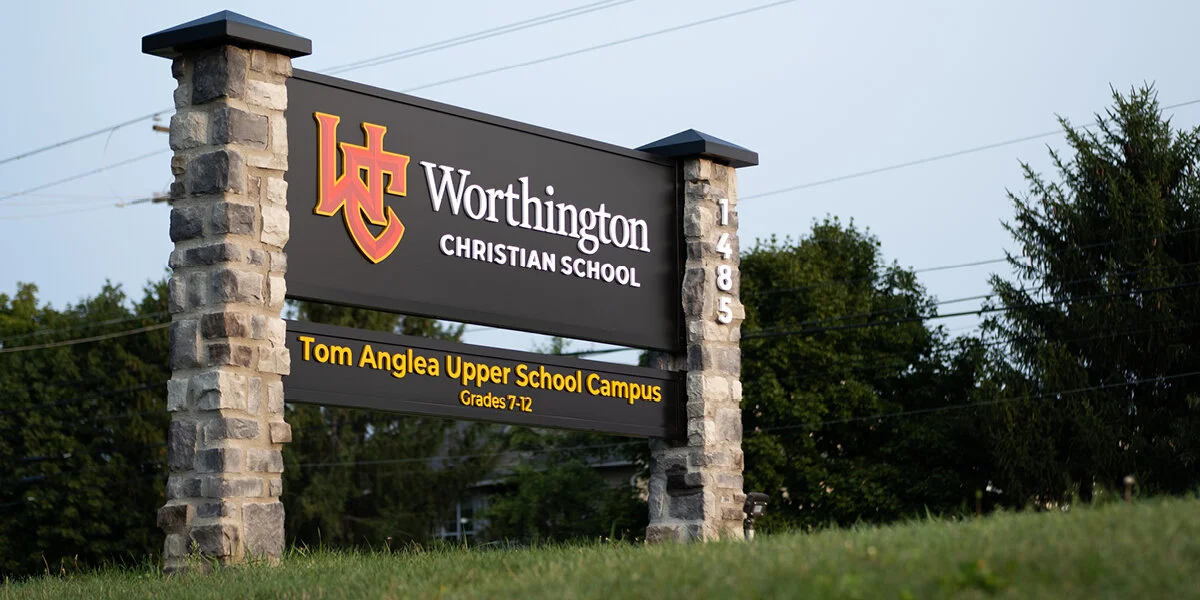 A stone and wood sign for Worthington Christian School, displaying the address 1485, with the school's logo and information about the Tom Anglea Upper School Campus for grades 7-12.