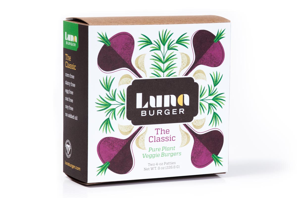Front of a Luna Burger plant-based veggie burger package with illustrations of beets, ginger, and herbs. The box is white with a black and green label, and black side panel listing product features.