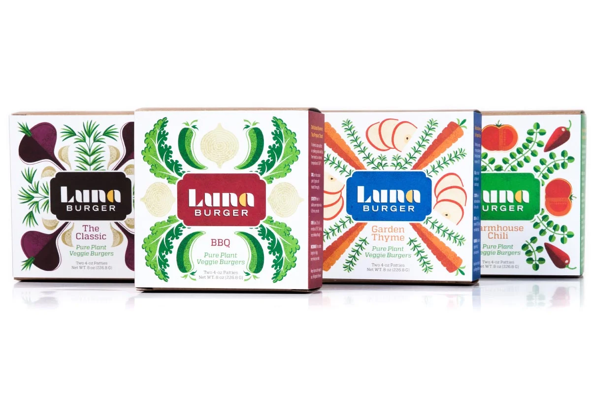 Four Luna Burger veggie burger boxes arranged in a row, each with colorful vegetable illustrations and the Luna Burger logo