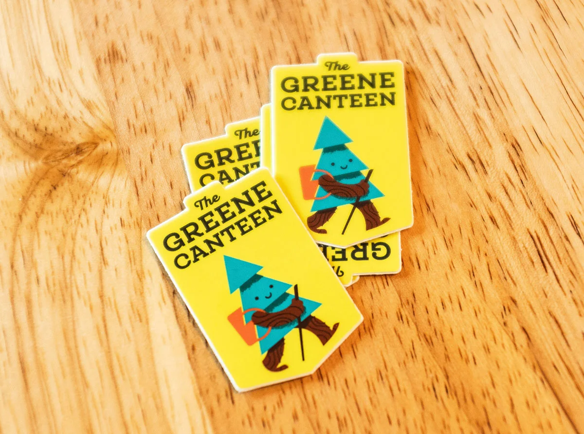 Four small stickers with yellow backgrounds featuring a cartoon camping character with a blue triangular hat, smiling face, and holding a hiking staff, labeled "The Greene Canteen."