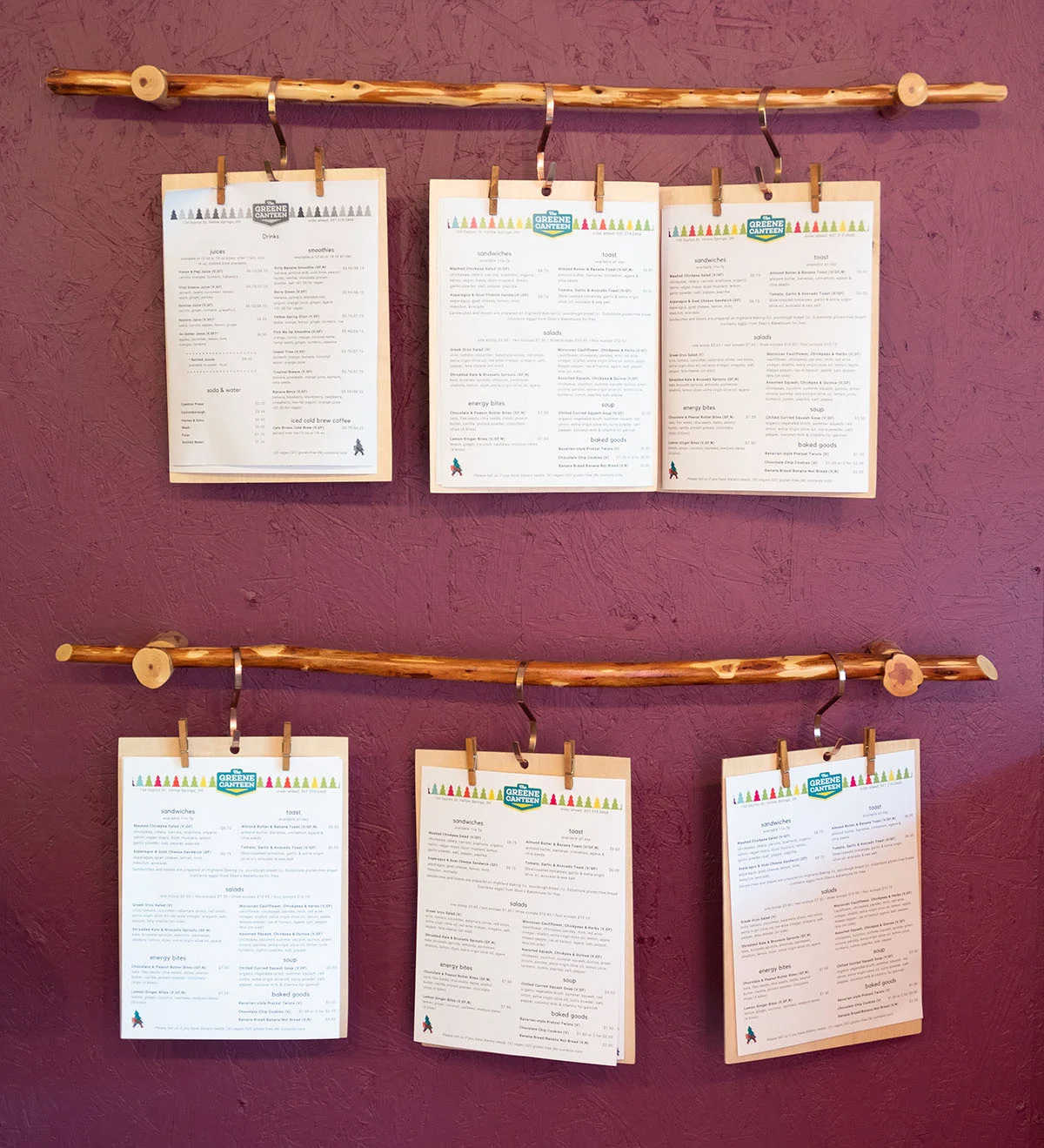 Menu boards hanging on a rustic wooden rod against a maroon textured wall.