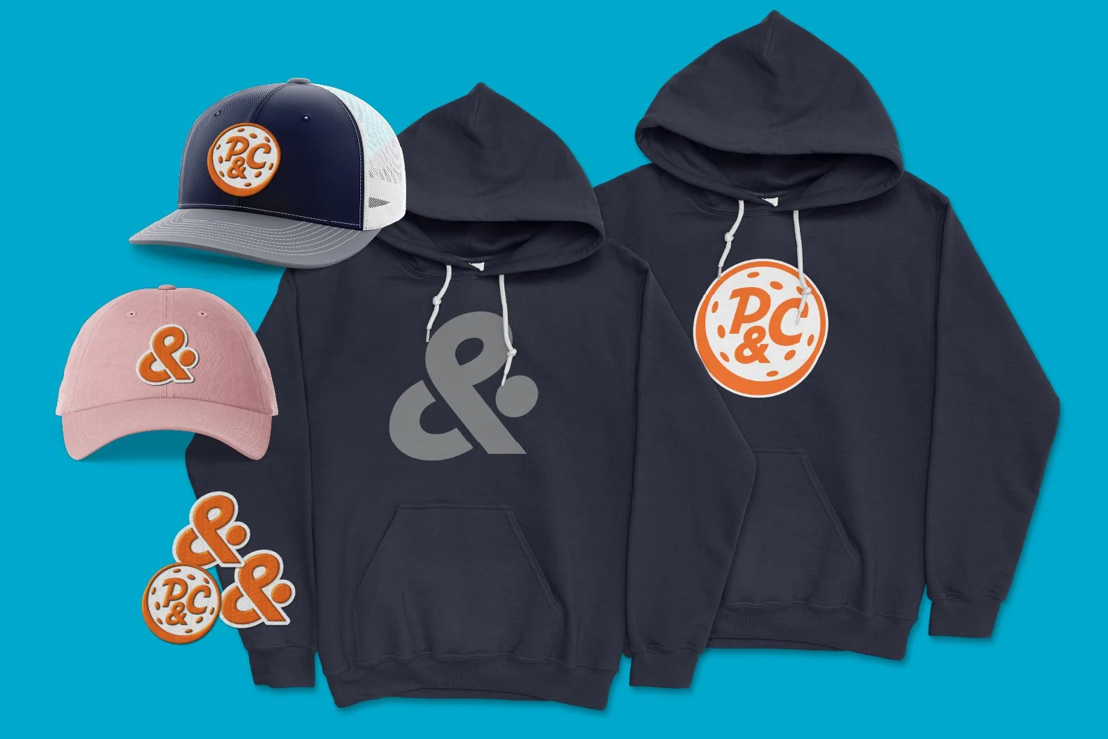 Two black hooded sweatshirts with large ampersand symbols, two caps with brand logos, and decorative stickers with brand logos on a blue background.