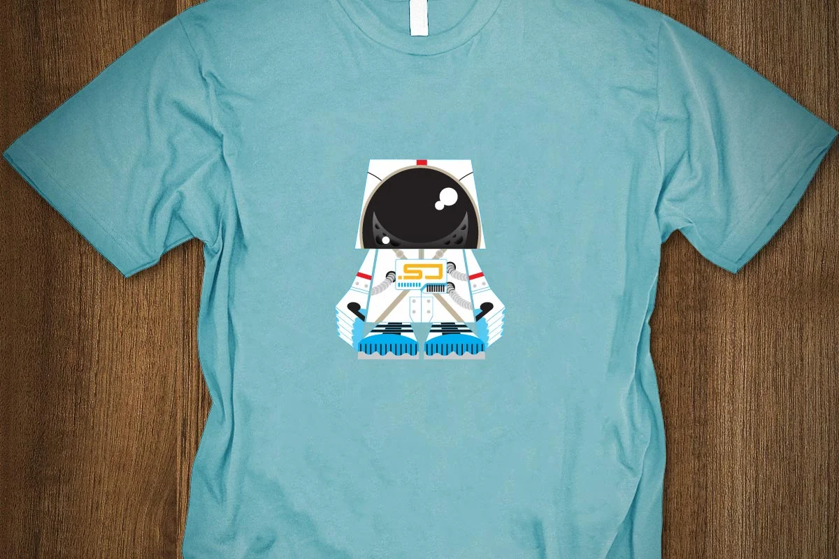 A light blue T-shirt with a cartoon astronaut graphic on the front, showing a stylized body with space suit details and a black helmet.