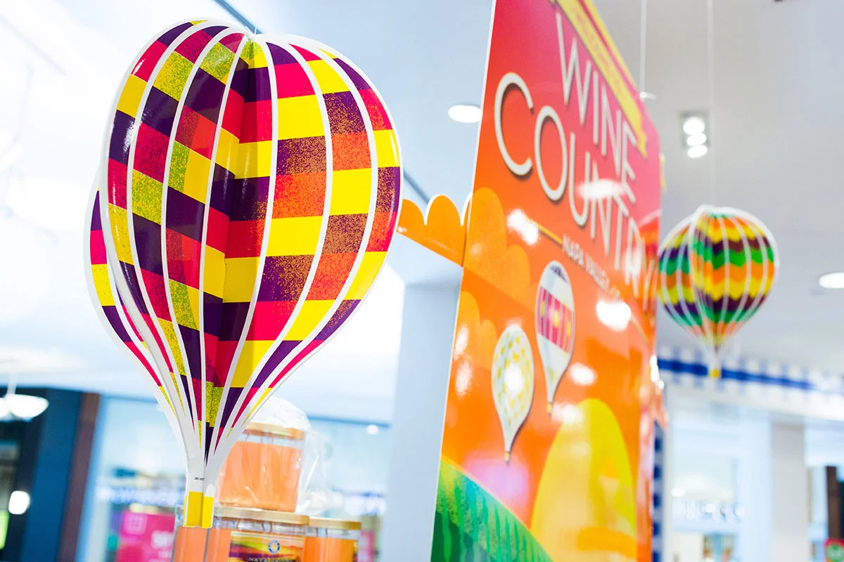 Colorful hot air balloon decorations with a sign promoting a wine, wine country, and hot air balloon theme at an indoor event.