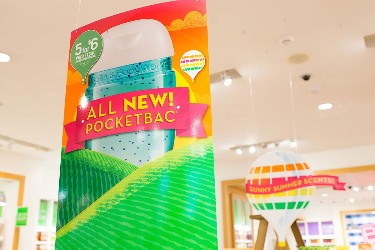 A colorful advertisement banner for a Pocketbac hand sanitizer displays the text "ALL NEW! POCKETBAC" in bold. The background features green, yellow, and orange fields with a white cap of the sanitizer visible at the top left corner.