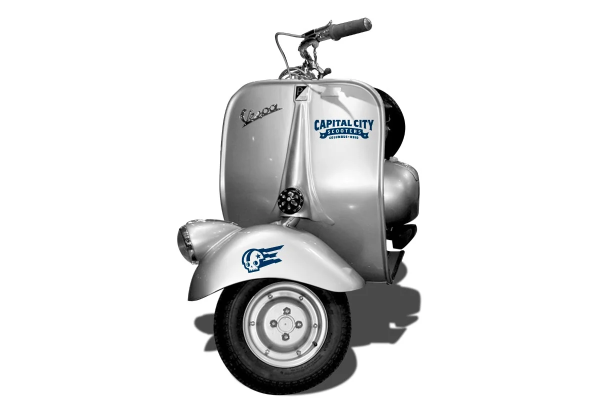 A silver Vespa scooter with a skull and ghost logo on the front fender, a 'Vespa' badge on the side, and a sticker that reads 'Capital City Scooters Columbus, Ohio'.