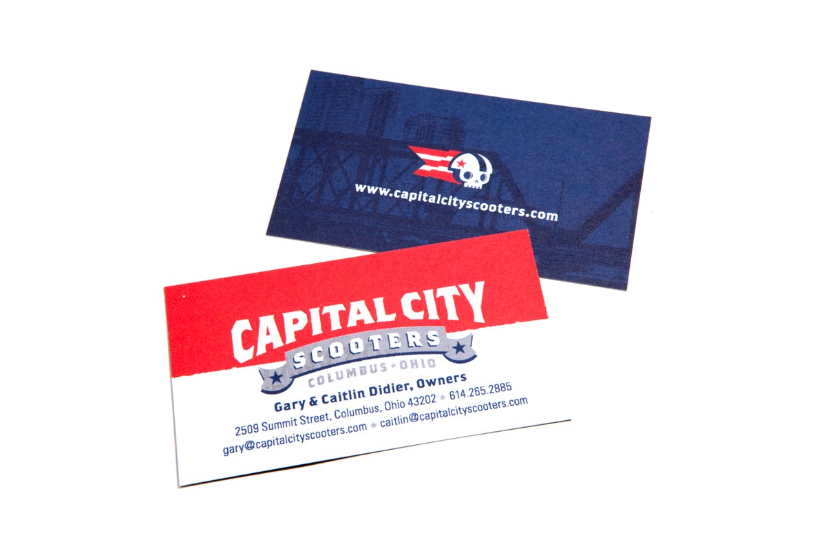 Business card for Capital City Scooters, featuring a red, white, and blue color scheme, with a logo of a skull and a star-spangled banner, and contact information including website, email, phone number, and address.
