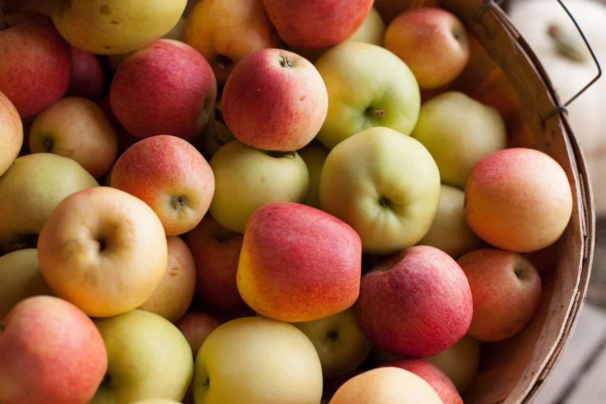 A basket filled with fresh apples in shades of red, yellow, and green.