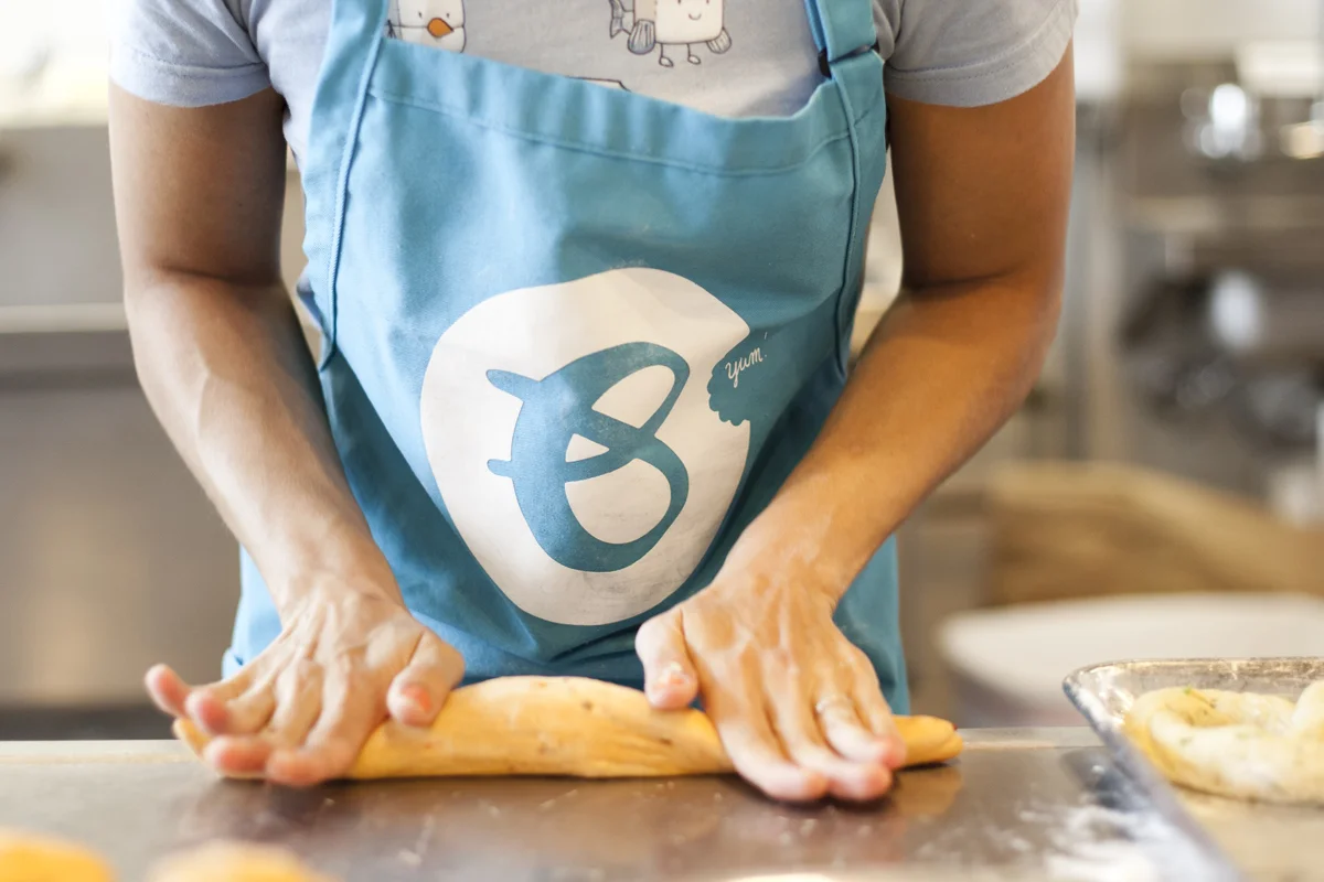 A person wearing a light blue apron and a T-shirt with cartoon characters is rolling out dough on a kitchen counter.