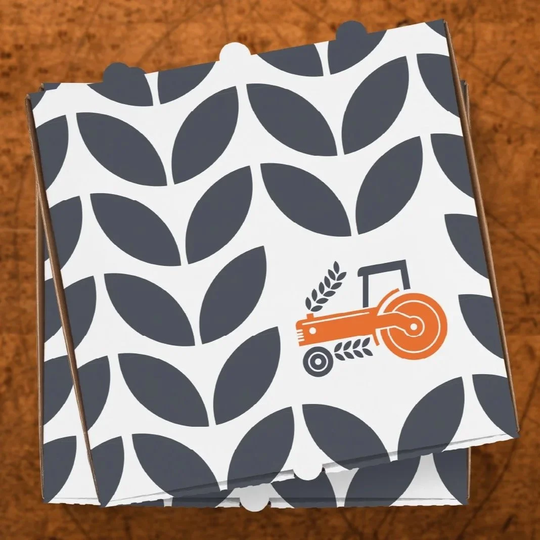 A cardboard box with a black and white leaf pattern and a logo of a red saw with wheat stalks, placed on a wooden surface.