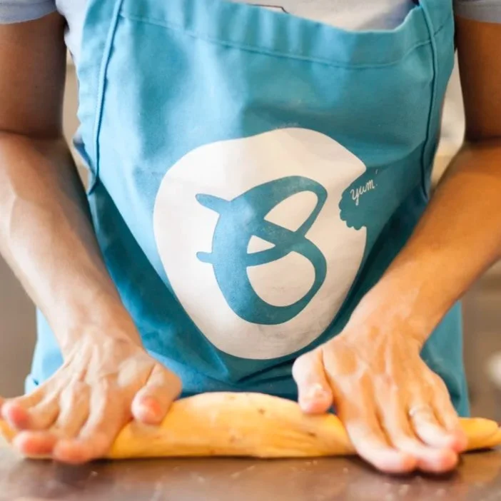 Person wearing a blue apron is rolling dough on a countertop.