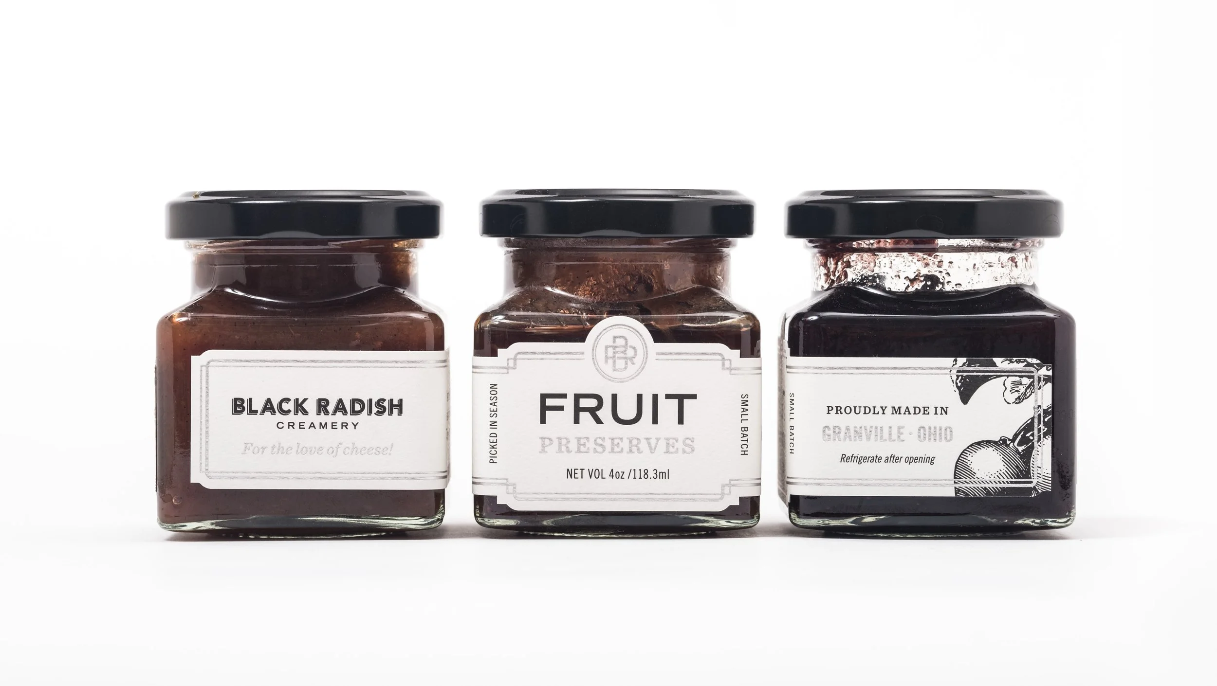 Three glass jars with black lids labeled 'Black Radish Creamery,' 'Fruit Preserves,' and 'Proudly Made in Granville Ohio,' aligned against a plain white background.