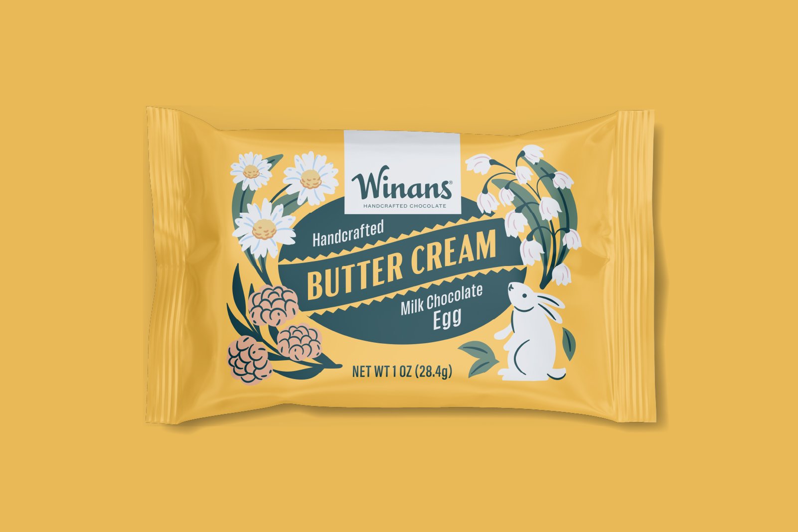 A yellow wrapper of Winans handcrafted chocolate, milk chocolate egg filled with butter cream. The wrapper features illustrations of flowers and a white bunny rabbit drawing. Packaging design and illustration by Slagle Design. 