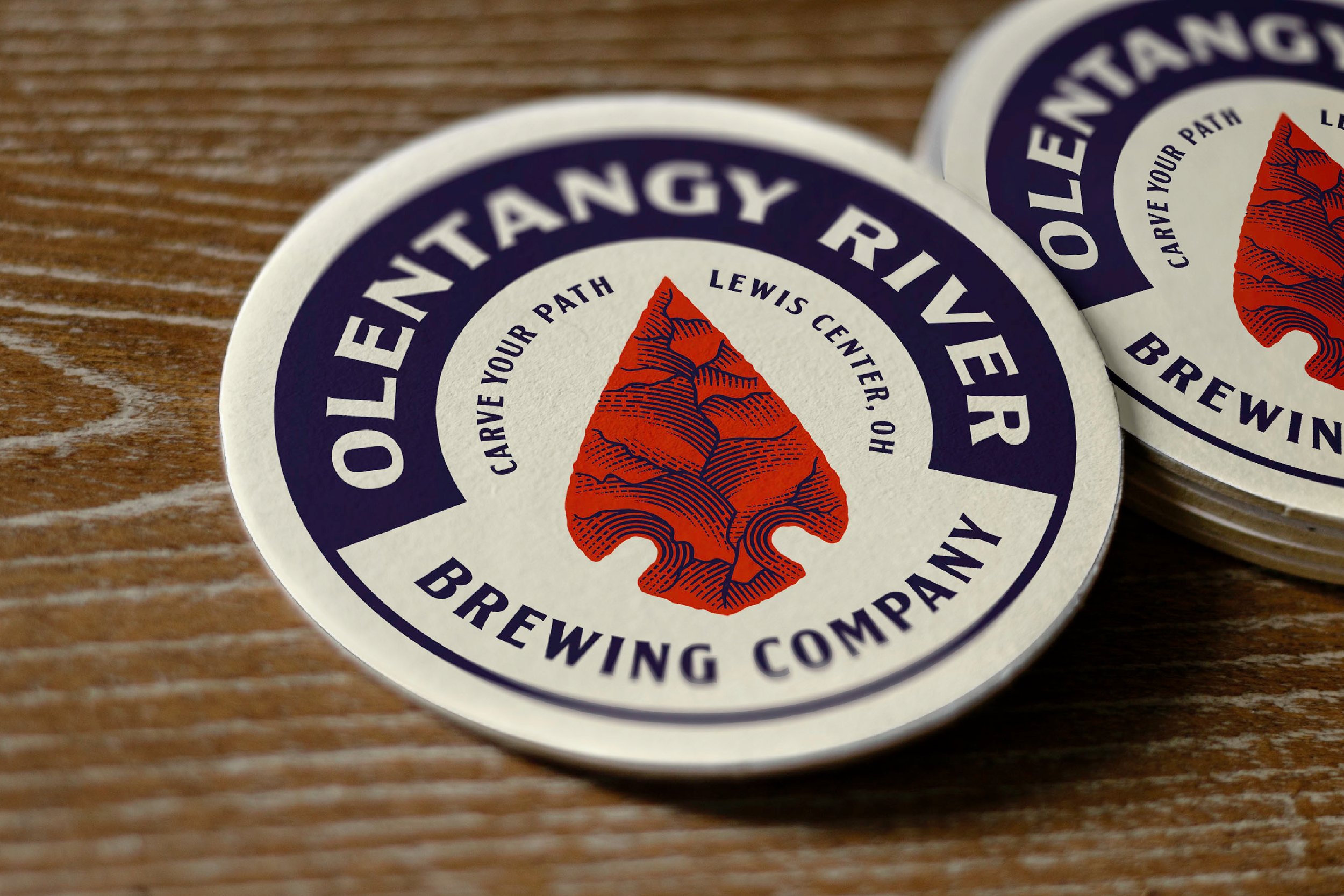 Close-up of circular stickers with a mountain logo in the center, reading 'Garvey Our Path Brewing Company' and 'Celebrate Your Path' on a wooden surface.