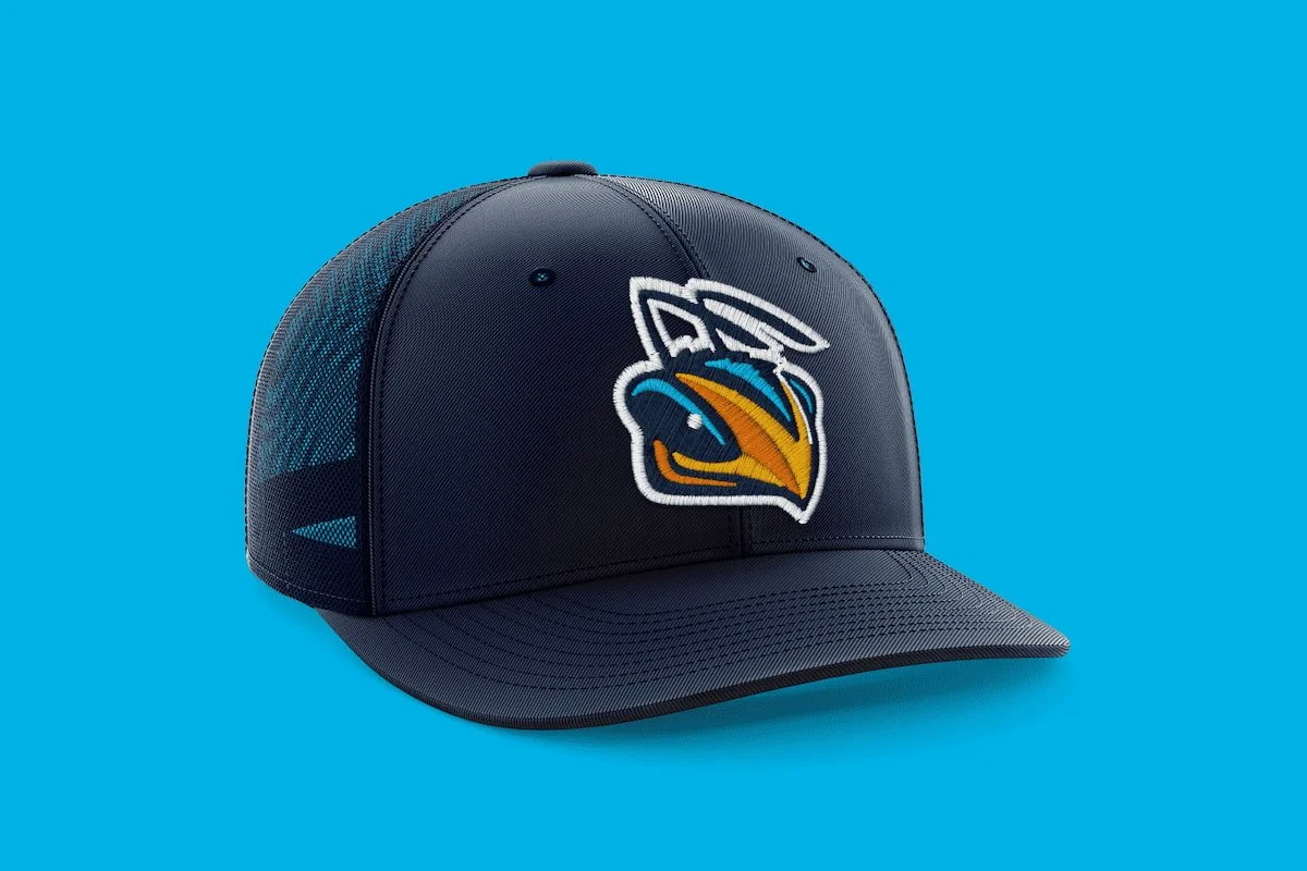A navy blue baseball cap with a colorful logo of a merlin bird on the front, resting on a bright blue background.