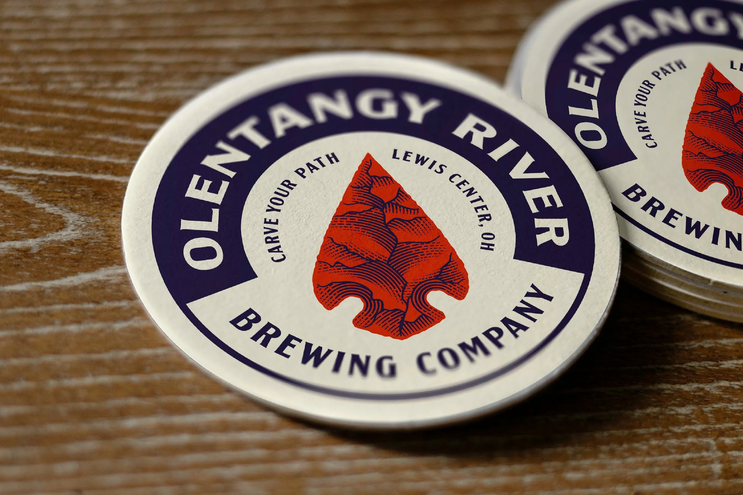 Close-up of circular stickers with a mountain illustration and text about a brewing company, placed on a wooden surface.