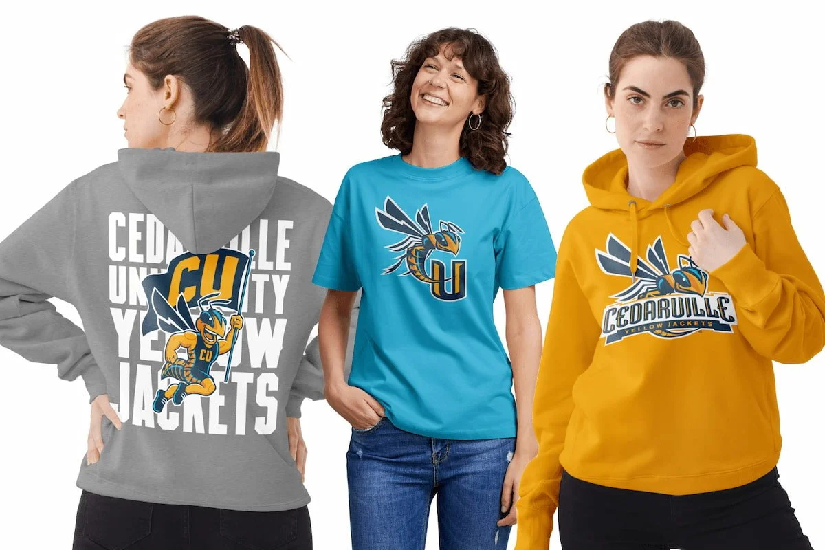 Three women modeling Cedarlale Yellow Jackets apparel: a woman in a gray hoodie with the team mascot and name on the back, a woman in a blue T-shirt with the team logo, and a woman in a yellow hoodie with the team logo and name.