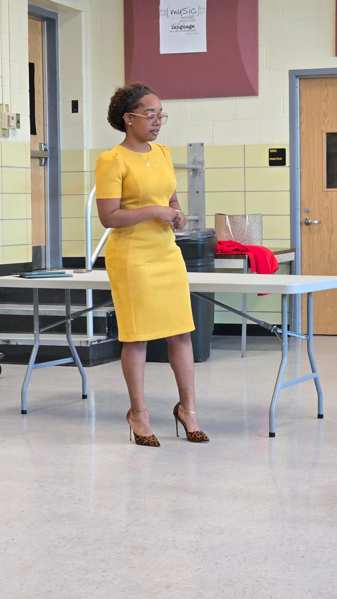 A woman in a yellow dress and leopard print high heels standing in a room with a table and a sign that reads "music is a world within itself with a language we all understand."