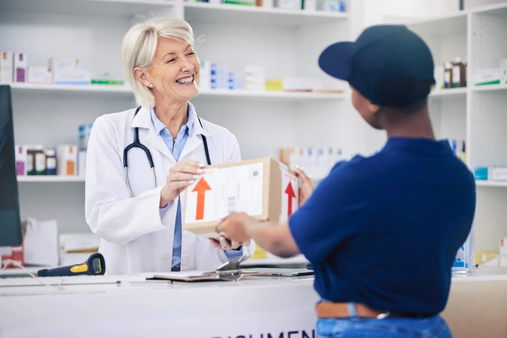 A smiling female pharmacist handing a package to a customer at the pharmacy counter.