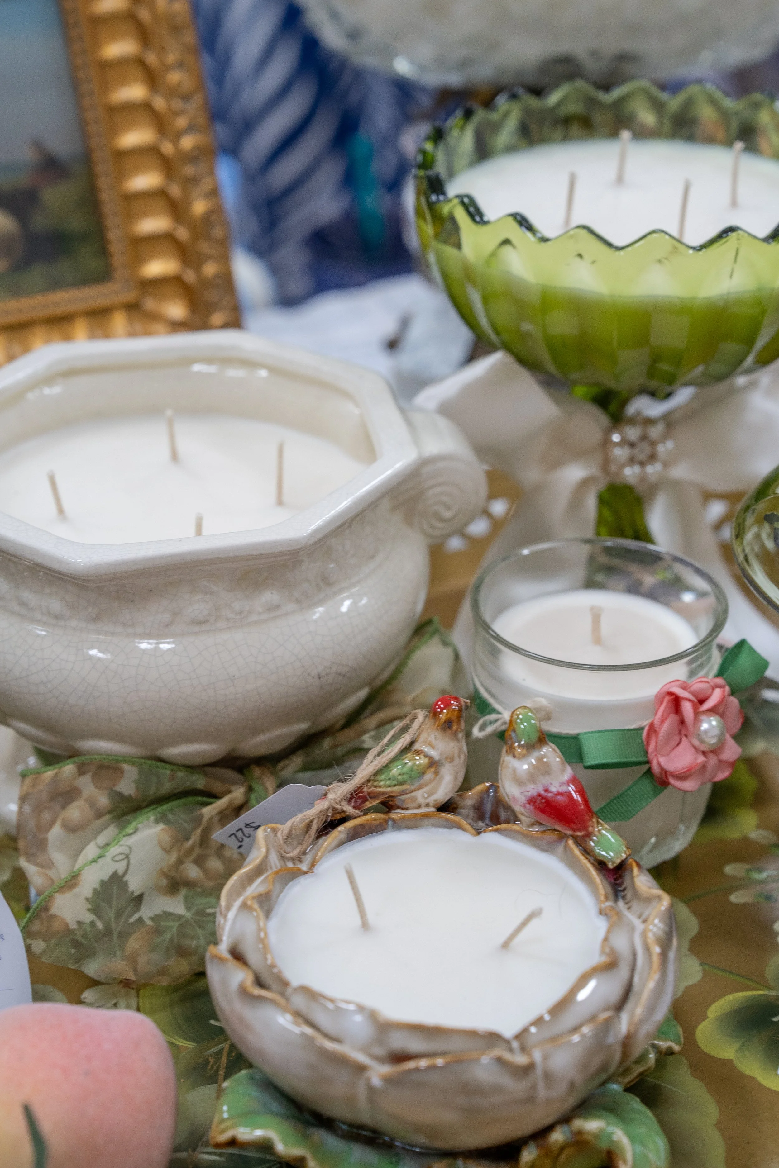 Decorative candles in ornate ceramic holders with floral and bird accents, arranged on a surface with other decorative items and greenery.