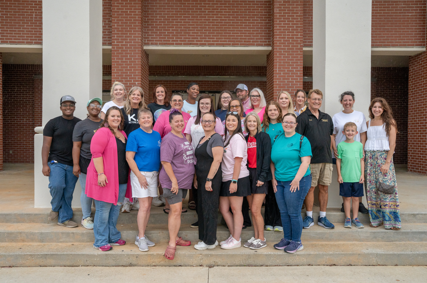 Group of diverse people gathered on outdoor steps, in front of a brick building, smiling for a photo.