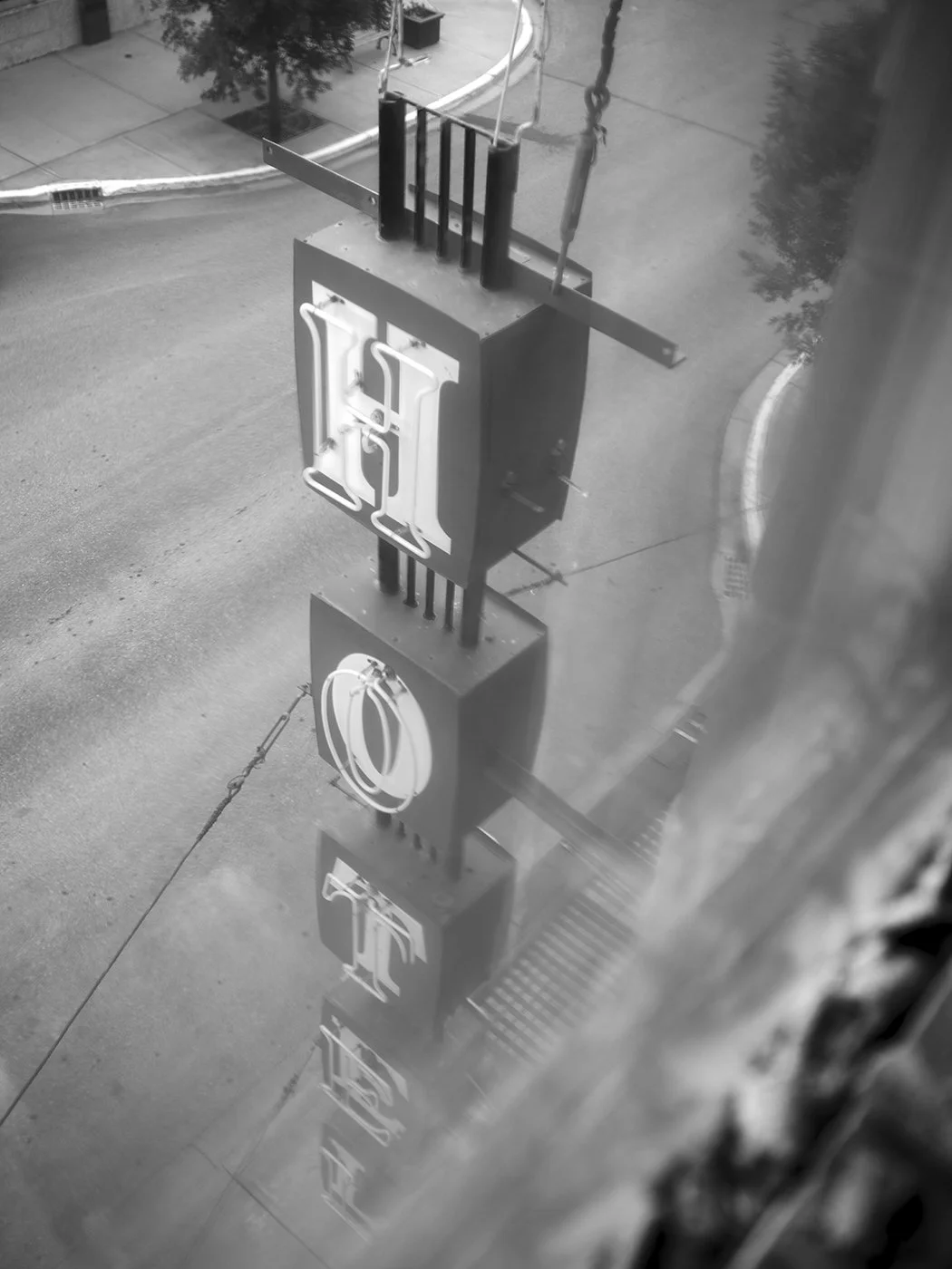 Reflection of a sign with the word "OPEN" in mirrors on the glass window looking onto a street with a sidewalk and trees.