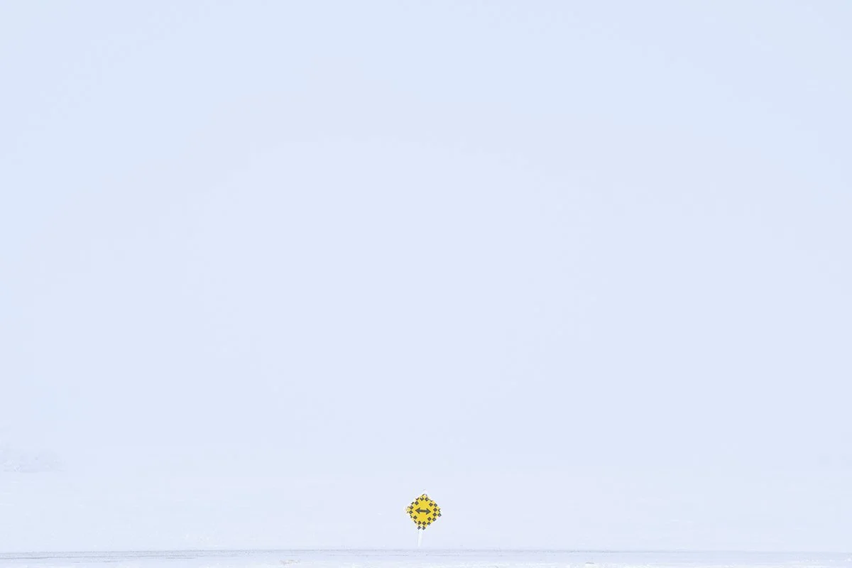 A snow-covered landscape with a clear, pale blue sky. In the distance, a small, bright yellow object or structure is visible on the snow.