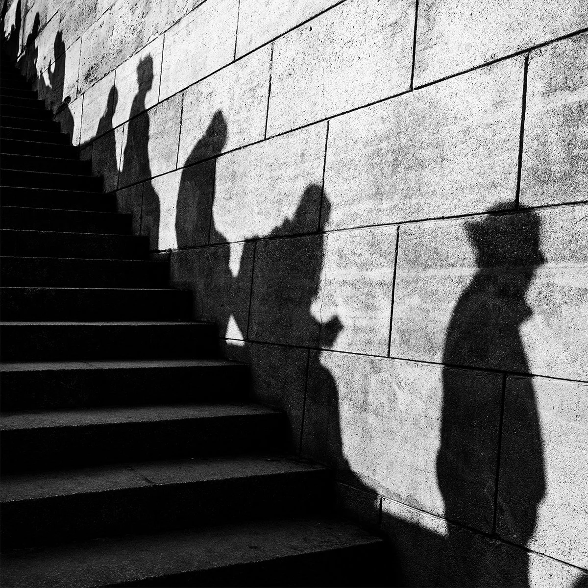 Shadow of a person walking up stairs and other people's shadows cast on a brick wall.