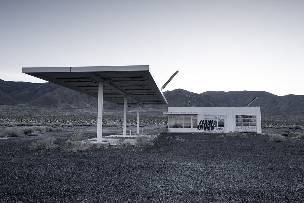 Abandoned building , abandoned gas station on a desert landscape, mountains in the background, and graffiti on the side of the building.