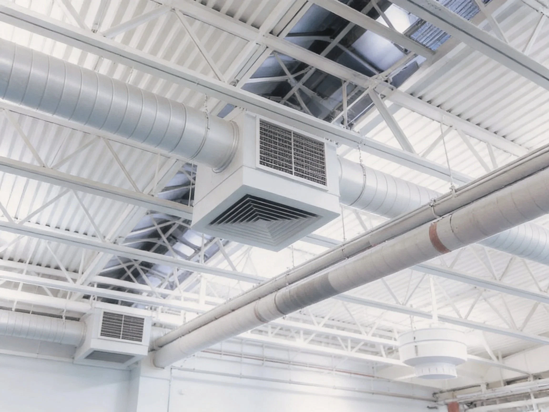 Ceiling with exposed white metal beams, large silver air ducts, and ceiling-mounted HVAC units in an industrial or commercial building.