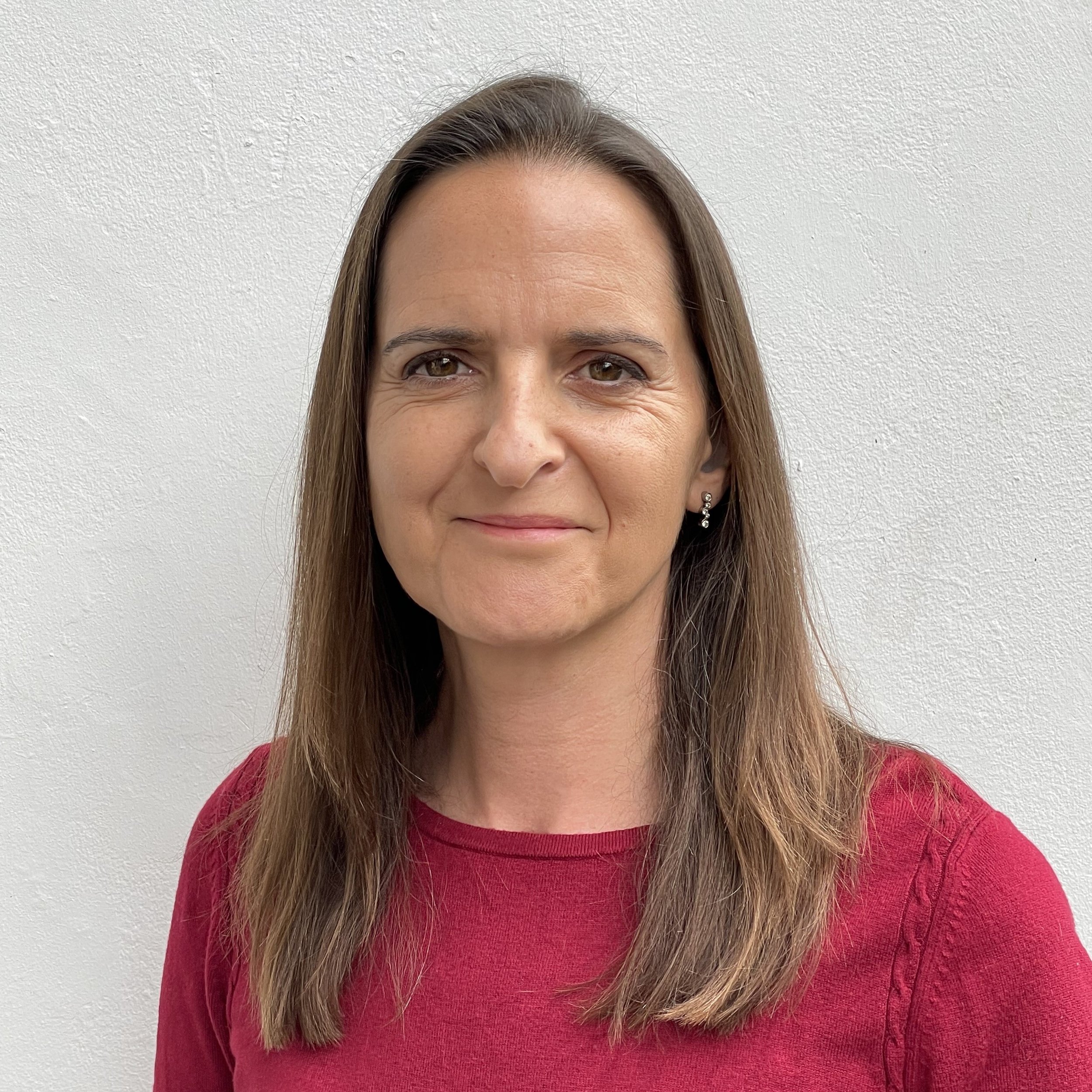 Photo of Claire, smiling. Long brown hair and red top