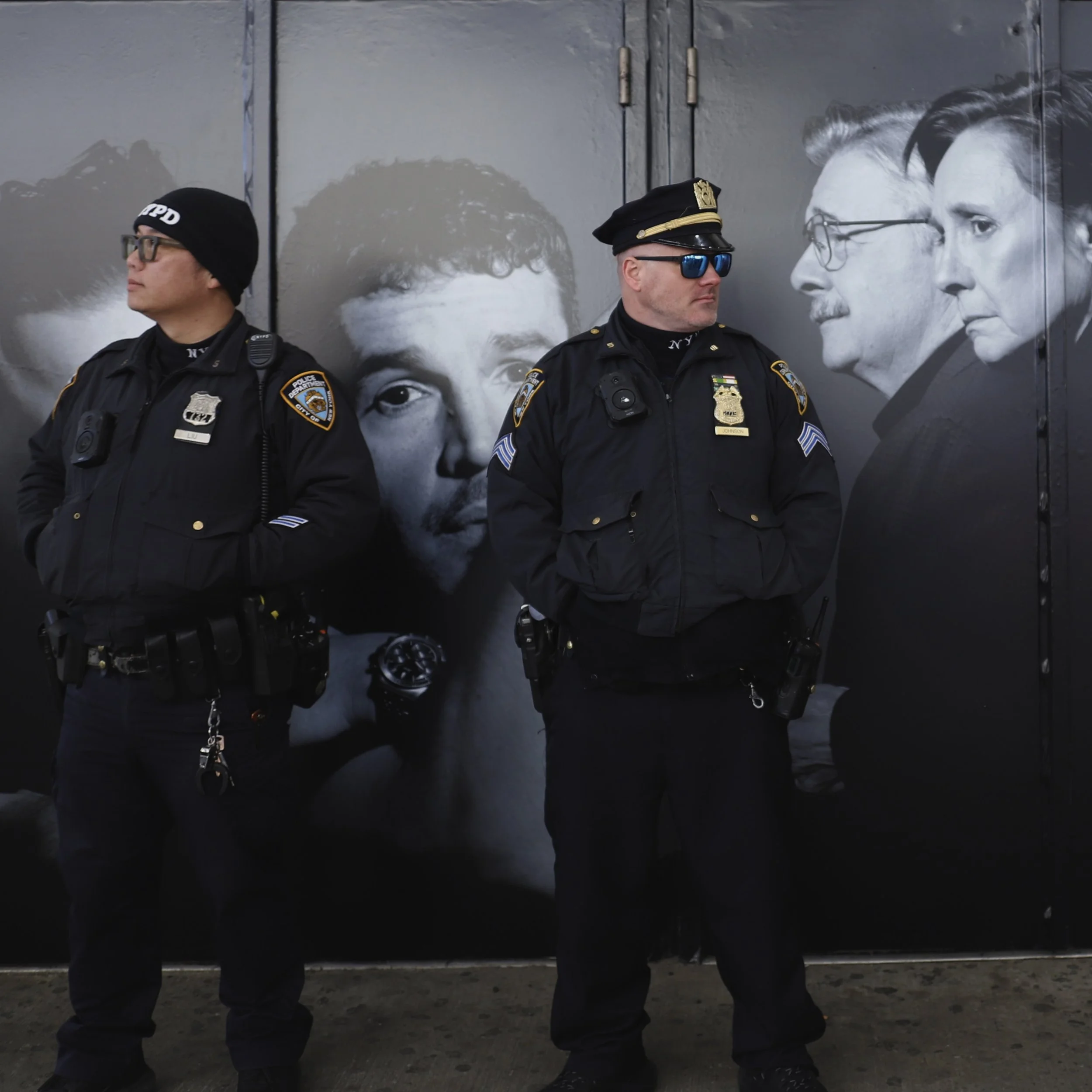 Two police officers standing in front of a wall with black-and-white images of people.