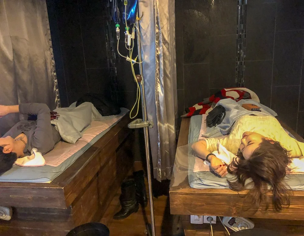 Two women lying on hospital beds with medical equipment and IV stands nearby.