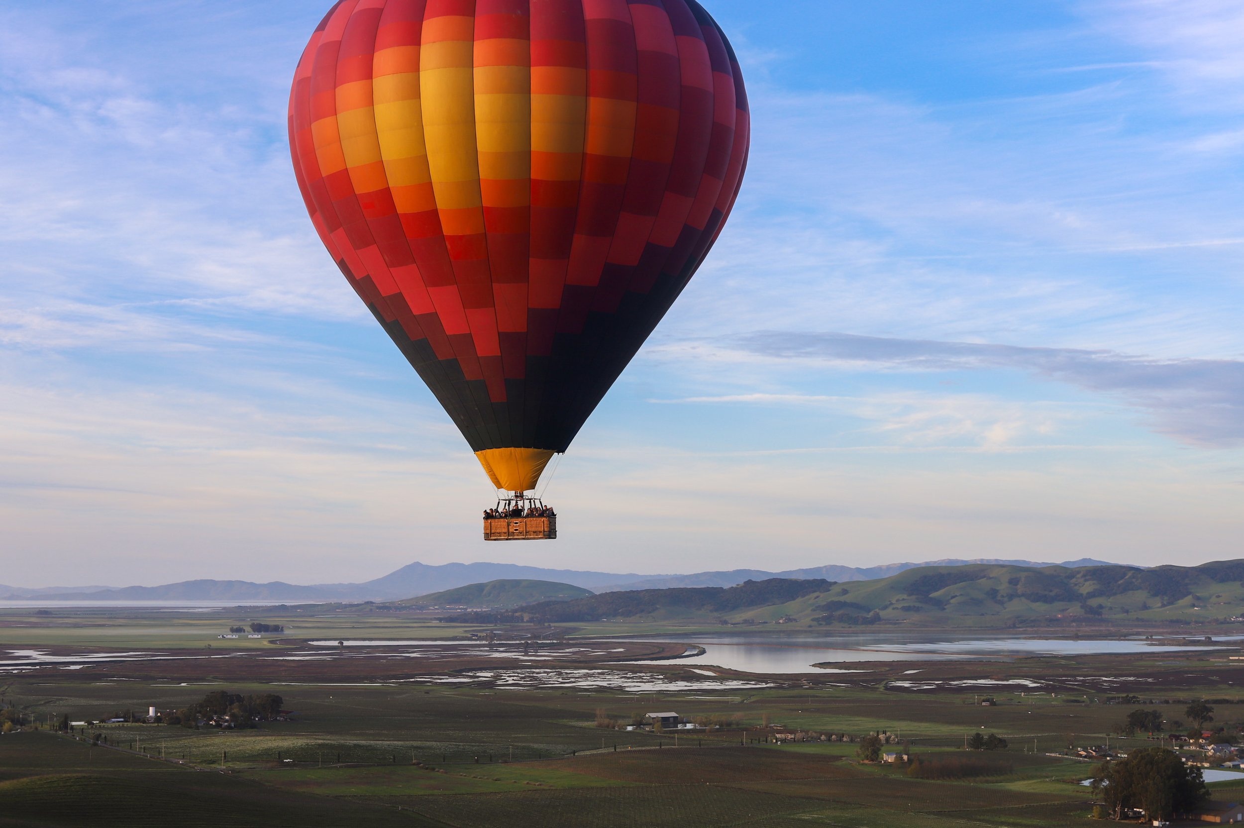 A colorful hot air balloon floating over a landscape with water, hills, and a cloudy sky.