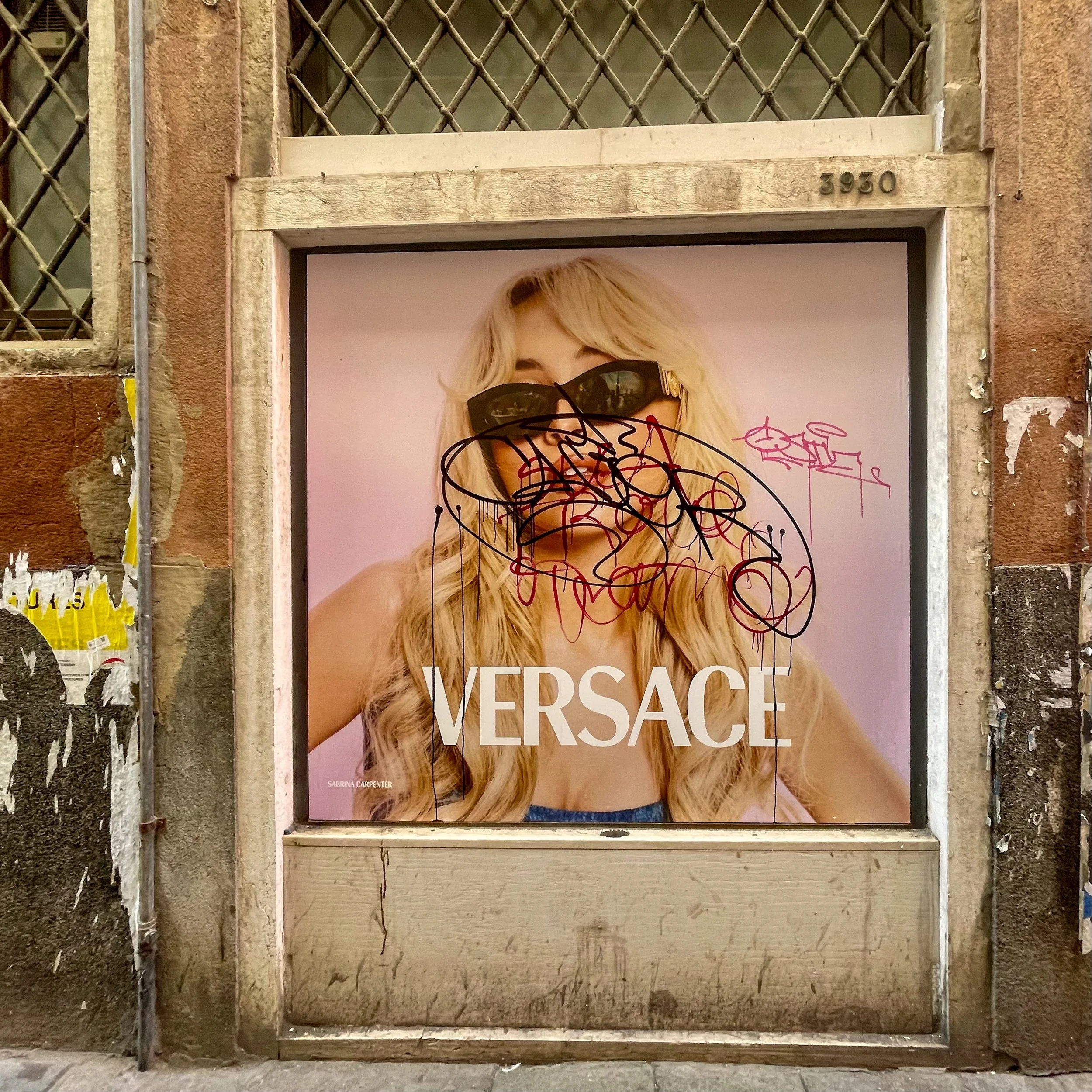 Versace advertisement featuring a blonde woman with long hair wearing black sunglasses, with scribbles over her face and the Versace logo at the bottom.